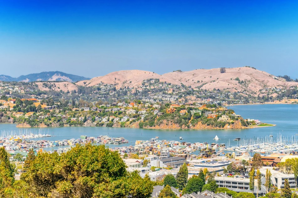 3 brown hills lined with trees and homes with water and boats surrounding them.